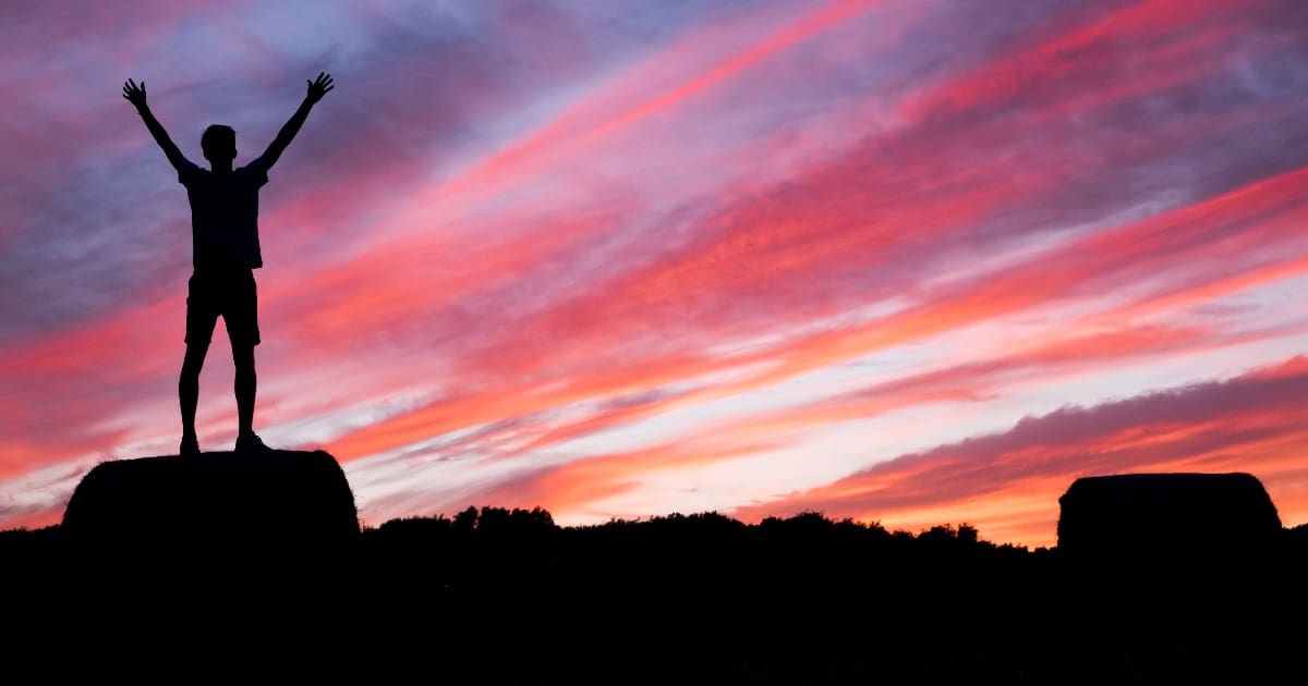 a silhouette of a person standing on top of an object outdoors with a sunset behind them